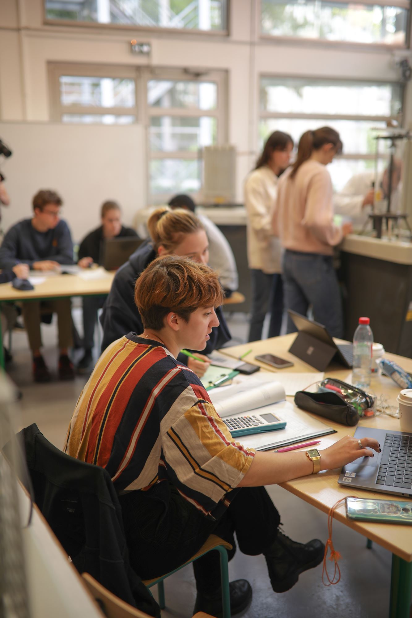 Des étudiantes en train de travailler autour d'une table avec ordinateur, cahier et calculatrice