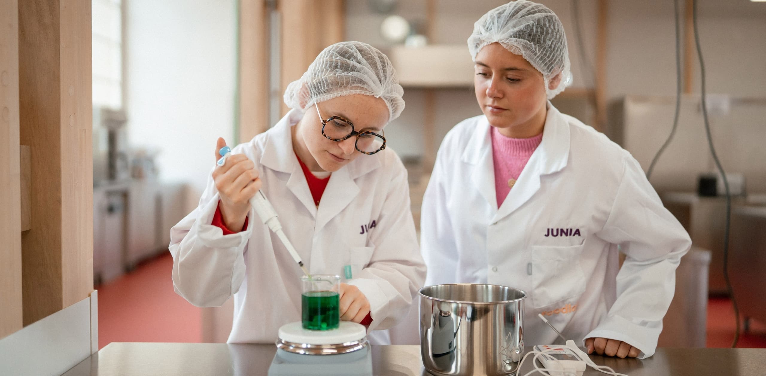 Etudiantes en laboratoire avec blouse et charlotte en train de manipuler pipette et contenant avec du liquide sur une paillasse